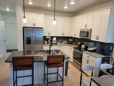 Kitchen featuring stainless steel appliances, white cabinets, decorative backsplash, dark stone countertops, and light wood-style floors