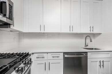 Kitchen featuring light countertops, backsplash, appliances with stainless steel finishes, white cabinetry, and a sink