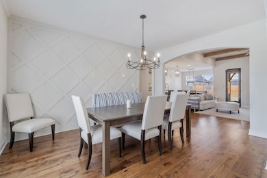 Dining area with light wood-style flooring, a chandelier, arched walkways, and crown molding