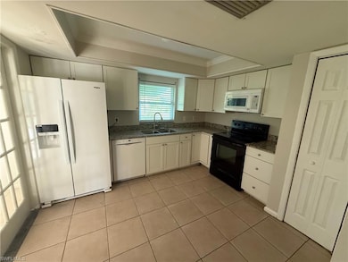 Kitchen featuring white appliances, light tile patterned floors, a raised ceiling, white cabinets, and ornamental molding