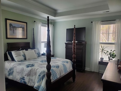 Bedroom with dark wood-style floors, ornamental molding, and a tray ceiling