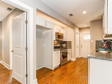 Kitchen with dark stone countertops, stainless steel appliances, light wood-type flooring, white cabinetry, and recessed lighting