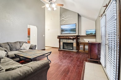 Living area featuring a fireplace, high vaulted ceiling, a ceiling fan, and wood finished floors