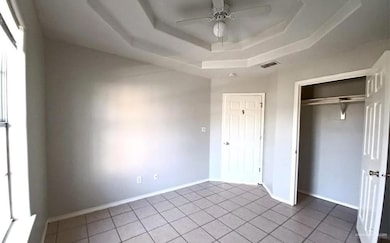 Unfurnished bedroom with tile patterned floors, a raised ceiling, a closet, and ceiling fan