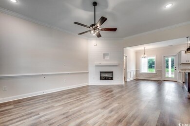 Unfurnished living room with ceiling fan with notable chandelier, a fireplace, crown molding, and wood finished floors
