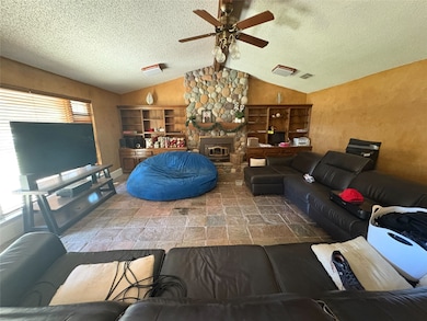 Living room featuring lofted ceiling, stone finish floors, ceiling fan, and a textured ceiling