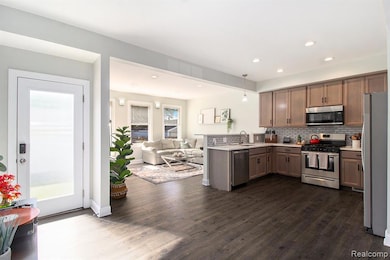 Kitchen featuring open floor plan, stainless steel appliances, decorative backsplash, pendant lighting, and dark wood-type flooring