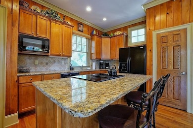 Kitchen featuring healthy amount of natural light, decorative backsplash, light stone countertops, ornamental molding, and brown cabinetry
