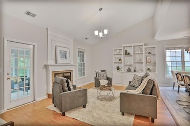 Living area with a chandelier, light wood-style flooring, a fireplace, and high vaulted ceiling