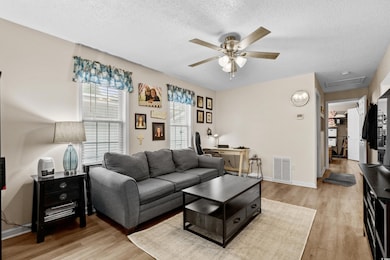 Living room with ceiling fan, light wood finished floors, a textured ceiling, a desk, and baseboards