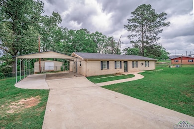 Ranch-style home with a detached carport, an outdoor structure, brick siding, driveway, and a front yard