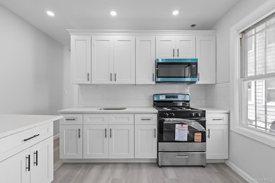 Kitchen with stainless steel gas range oven, white cabinetry, backsplash, light wood-style flooring, and recessed lighting