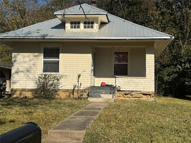 Bungalow-style home with a front yard, covered porch, and a metal roof