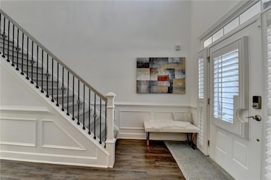 Foyer entrance with wood finished floors, a decorative wall, stairs, a wainscoted wall, and a towering ceiling