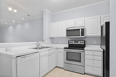 Kitchen with appliances with stainless steel finishes, light countertops, crown molding, white cabinets, and light tile patterned floors