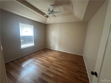 Spare room with a tray ceiling, wood finished floors, a ceiling fan, and baseboards