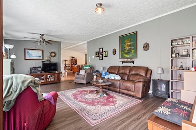 Living room with wood finished floors, a textured ceiling, ceiling fan, a wood stove, and crown molding
