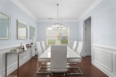 Dining room with a chandelier, crown molding, a decorative wall, and a wainscoted wall