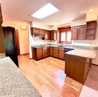 Kitchen featuring black appliances, a peninsula, under cabinet range hood, open shelves, and a chandelier