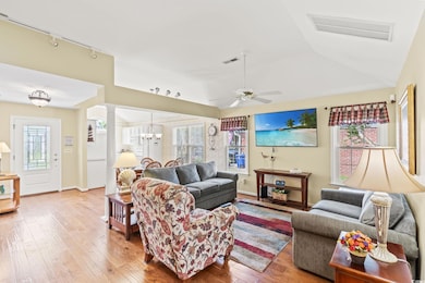 Living room featuring hardwood / wood-style flooring, rail lighting, ornate columns, vaulted ceiling, and ceiling fan