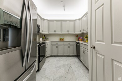 Kitchen with appliances with stainless steel finishes, light marble finish floors, light countertops, gray cabinets, and backsplash