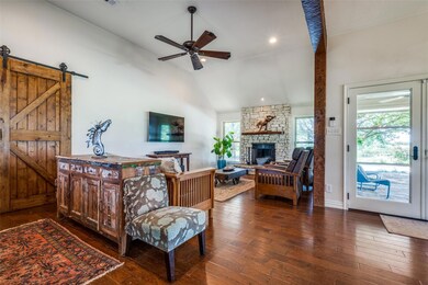 Living room with high vaulted ceiling, dark hardwood / wood-style floors, a barn door, a stone fireplace, and ceiling fan