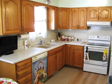 Kitchen featuring white electric range, under cabinet range hood, a sink, dishwashing machine, and brown cabinetry