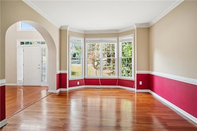 Spare room with healthy amount of natural light, arched walkways, light wood finished floors, and ornamental molding
