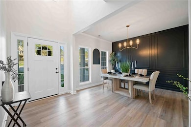 Foyer entrance featuring light wood-style flooring, a chandelier, ornamental molding, and baseboards
