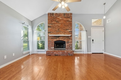 Living room featuring lofted ceiling, a fireplace, ceiling fan, and hardwood floors.