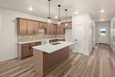 Kitchen with brown cabinets, decorative light fixtures, tasteful backsplash, an island with sink, and light wood-type flooring