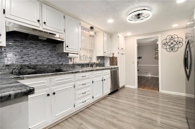 Kitchen with light wood-style floors, white cabinetry, tasteful backsplash, under cabinet range hood, and a textured ceiling