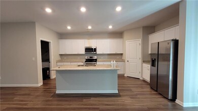 Kitchen with appliances with stainless steel finishes, white cabinets, a kitchen island with sink, dark wood-type flooring, and recessed lighting