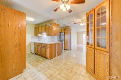 Kitchen with light countertops, ceiling fan, backsplash, glass insert cabinets, and brown cabinets