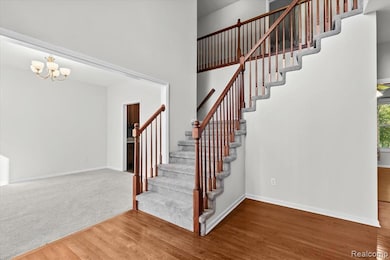 Stairway with a towering ceiling, wood finished floors, and a chandelier