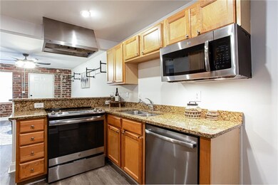 Kitchen featuring appliances with stainless steel finishes, wall chimney exhaust hood, a peninsula, dark wood-style flooring, and a sink