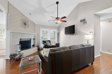 Living area featuring wood-like finished floors, a textured ceiling, a brick wood burning fireplace with raised hearth, high vaulted ceiling & ceiling fan
