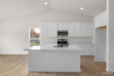 Kitchen with lofted ceiling, white cabinetry, stainless steel appliances, light countertops, and a kitchen island with sink
