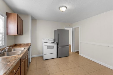 Kitchen featuring appliances with stainless steel finishes, brown cabinetry, light tile patterned flooring, and a textured ceiling