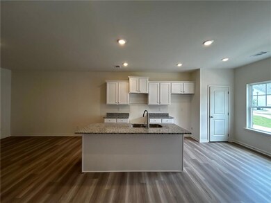 Kitchen with dark wood-type flooring, white cabinets, a center island with sink, stone countertops, and recessed lighting