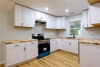 Kitchen with stainless steel range with electric cooktop, light wood-style flooring, white cabinetry, wood counters, and recessed lighting