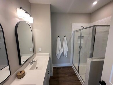 Bathroom featuring a shower stall, wood finished floors, and double vanity