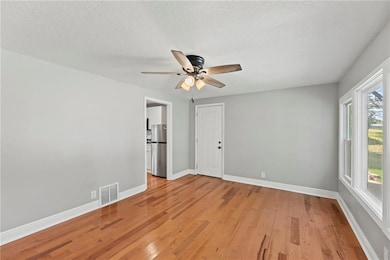 Empty room with light wood-type flooring, a ceiling fan, and a textured ceiling