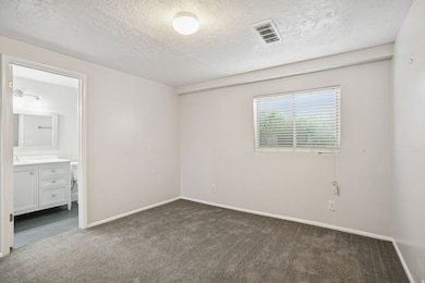 Unfurnished bedroom featuring dark colored carpet, a textured ceiling, and ensuite bath