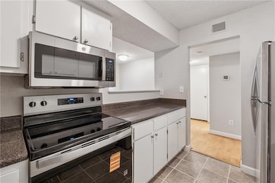 Kitchen featuring stainless steel appliances, dark countertops, white cabinetry, a textured ceiling, and light tile patterned floors