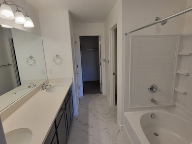 Full bath featuring double vanity, tub / shower combination, a spacious closet, and light marble finish floors