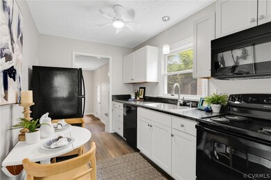 Kitchen featuring ceiling fan, white cabinetry, black appliances, dark wood-type flooring, and sink