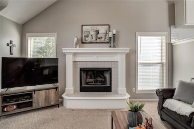 Living area featuring carpet flooring, a tile gas fireplace, and vaulted ceiling