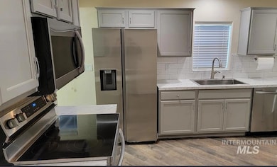 Kitchen featuring gray cabinets, stainless steel appliances, light wood finished floors, and backsplash