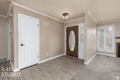 Foyer featuring crown molding, a fireplace with flush hearth, and light wood-type flooring